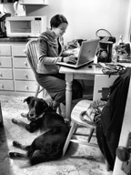 Foto de una chica riéndose delante de un portátil y un perro a su lado.