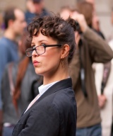 Foto de una mujer representando a una secretaria o asistente a la dirección, con pelo recogido, traje de chaqueta y gafas.