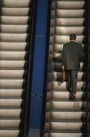 Escaleras mecánicas de subir y bajar por las que está subiendo un hombre de negocios. Flecha roja de una dirección es junto a la flecha azul ligera.