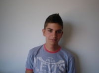 En la foto se ve el busto de un joven con camiseta gris con letras blancas mirando de frente a la cámara.