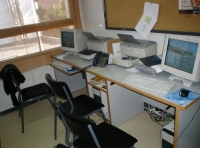 Se observan dos puestos de trabajo sin personal.  Estos puestos constan de silla, mesa, ordenador, impresora y un corcho al fondo para pinchar notas.