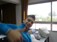 En la foto se ve a un joven sentado y diciendo ok con el pulgar de su mano derecha a la cámara.  El chivo va vestido de azul.