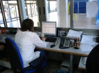 Se observa a una administrativa desde la parte posterior sentada frente a su puesto de trabajo.