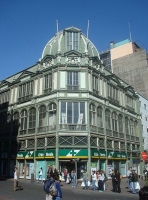 Se observa un gran edificio de estilo neoclásico de una gran compañía que hace esquina con dos calles. 