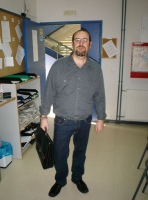 Un administrativo repasa un listado.  Se observa a un administrativo de pie y visto de frente, el cual porta un maletín en su mano derecha.