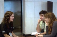 En la imagen se observa a una entrevistadora y dos jóvenes en frente, todos sentados al rededor de una mesa en un despacho.  Los jóvenes escuchan con atención.