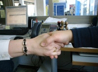 Se observan las manos de dos personas fundiéndose en un saludo. Están dentro de una oficina y al fondo se ve la pantalla del ordenador. 