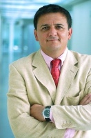 Se muestra un ejecutivo con chaqueta blanca y corbata de brazos cruzados mirando de frente a la cámara.